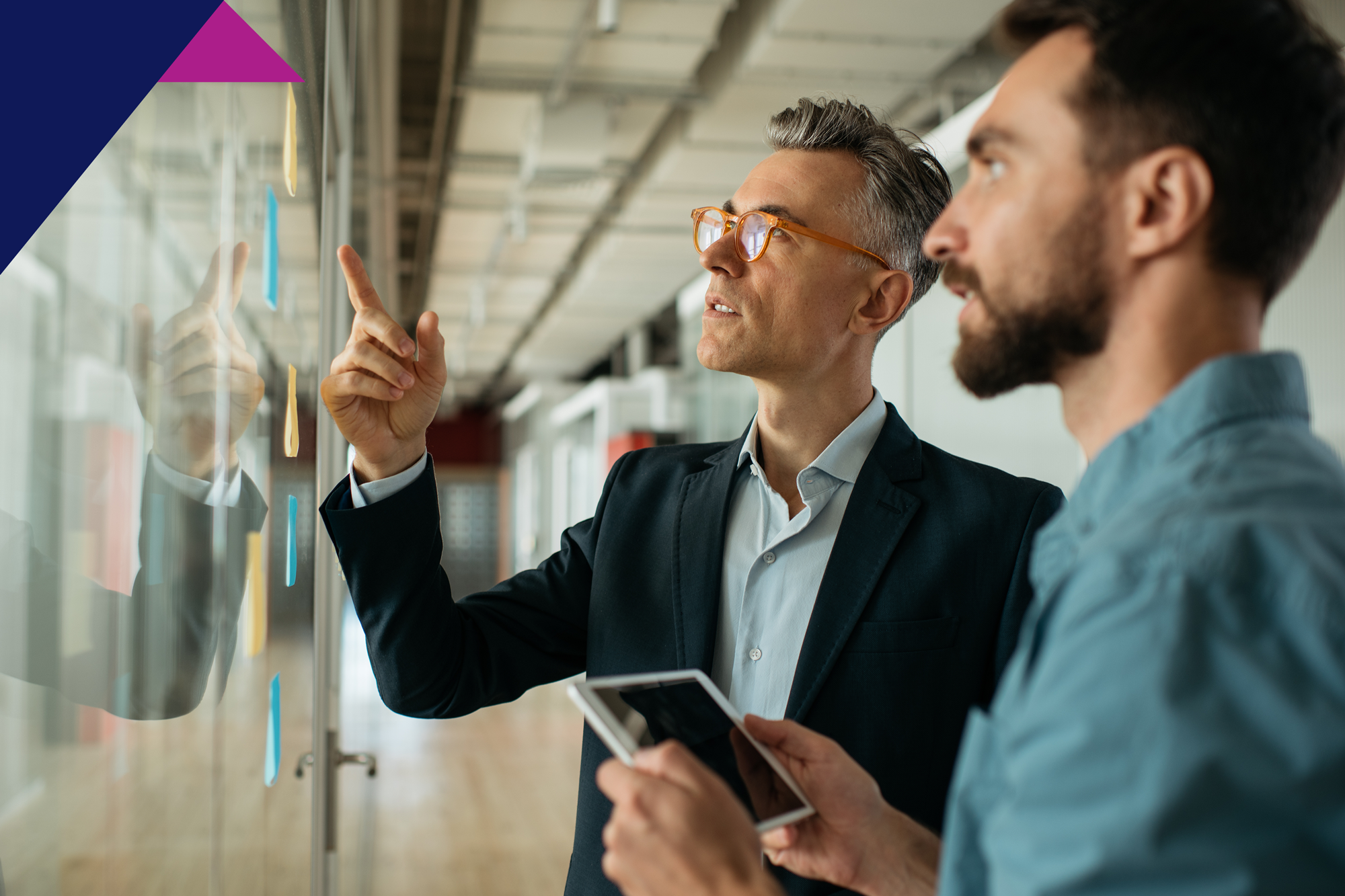 Man standing with a co-worker and pointing at a board with post-it notes